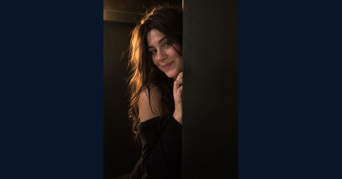 Example of a warm natural phone portrait of an adult woman peeking from behind a black partition